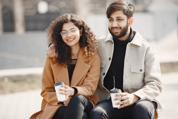 European girl anindian guy ride scooters and smile.  People with coffee.