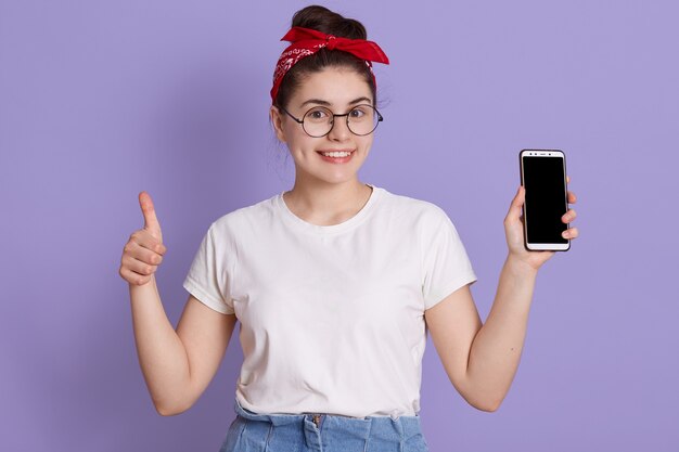 European girl showing blank cellphone screen and showing thumb up while looking happily