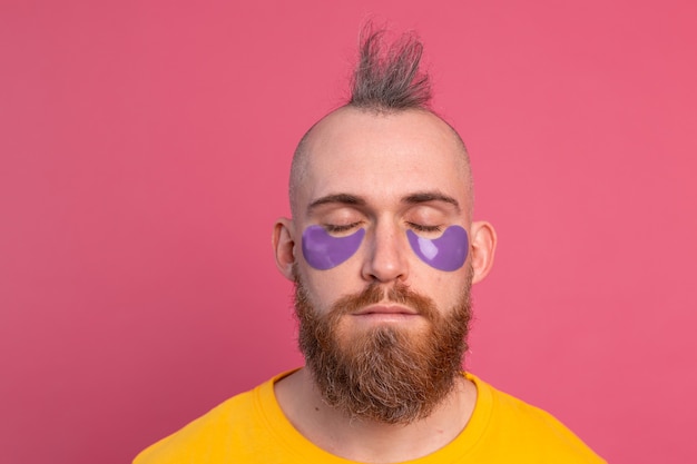 Европейский красивый бородатый мужчина в желтой футболке и фиолетовой маске для глаз на розовом
