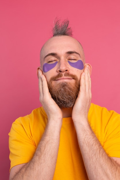 European handsome bearded man in yellow t-shirt and purple eye patches mask on pink