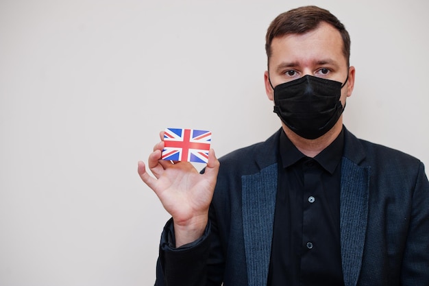 無料写真 ヨーロッパ人男性は黒のフォーマルを着用し、フェイスマスクを保護します白い背景に分離されたイギリスの旗カードを保持しますヨーロッパコロナウイルスcovid国の概念
