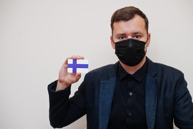 Foto gratuita l'uomo europeo indossa una maschera nera formale e protegge il viso, tiene la carta della bandiera della finlandia isolata su sfondo bianco europa coronavirus covid concetto di paese