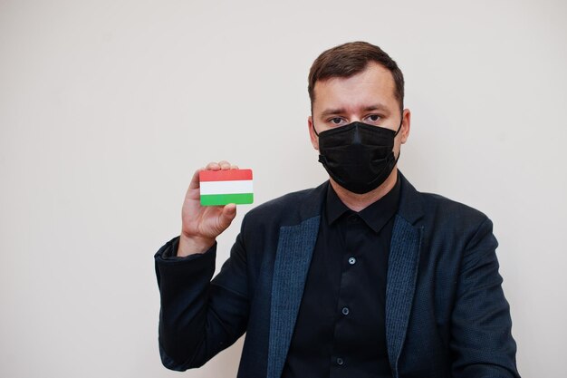 유럽 남성은 검은색 정장을 입고 얼굴 마스크를 보호하며 유럽 코로나바이러스 코비드 국가 개념에 격리된 헝가리 국기 카드를 들고 있습니다.