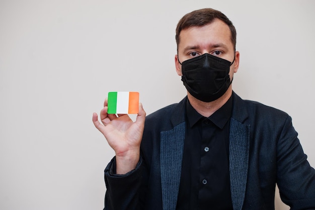 Foto gratuita l'uomo europeo indossa una maschera nera formale e protegge il viso tiene la carta bandiera irlandese isolata su sfondo bianco europa coronavirus covid concetto di paese