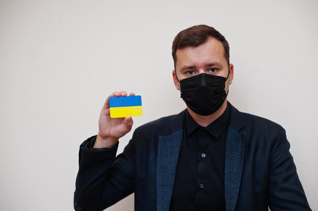 유럽 남성은 검은색 정장을 입고 얼굴 마스크를 보호하며 유럽 코로나바이러스 코비드 국가 개념에 격리된 우크라이나 국기 카드를 들고 있습니다.