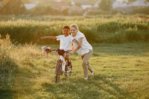 Европейская мать и африканский сын. Семья в летнем парке. Малыш с велосипедом.