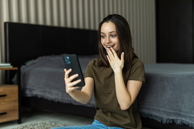 European smiling woman using mobile phone while sitting on floor at home
