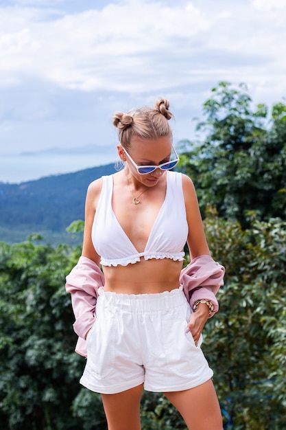 Free photo european stylish woman blogger tourist stands on the top of mountain with amazing tropical view of koh samui island thailand fashion outdoor portrait of female