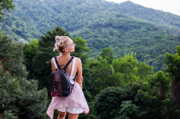 European stylish woman blogger tourist stands on the top of mountain with amazing tropical view of Koh Samui island Thailand Fashion outdoor portrait of female