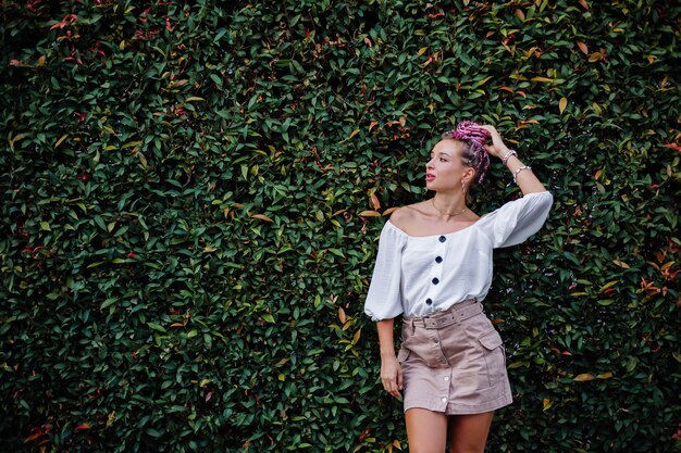 European stylish woman with pink colorful summer braids in beige skirt and white blouse