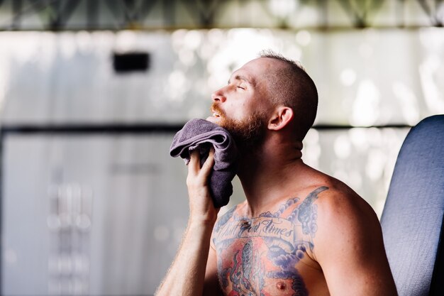 Европейский татуированный бородатый измученный, сильный усталый мужчина выглядит вспотевшим после тренировки