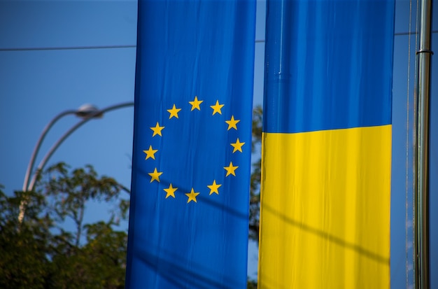 Флаг европейского союза и украинский флаг развевается на фоне голубого неба