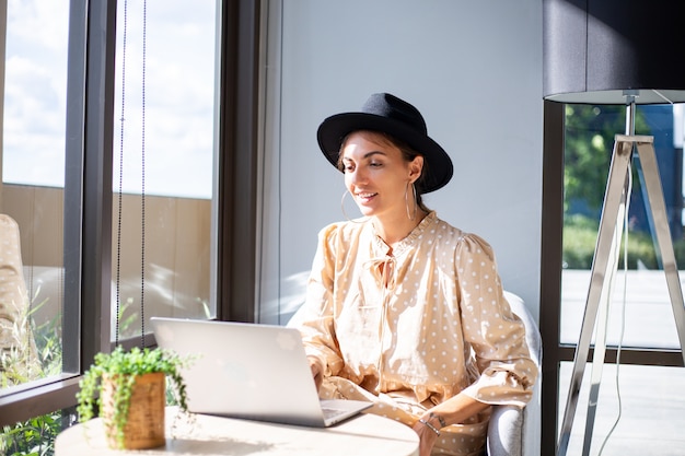 European woman in dress and classic hat works at home in kitchen