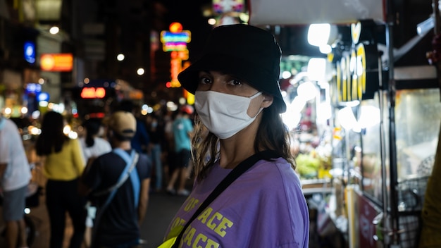 European woman in medical white face mask in crowded china town in bangkok