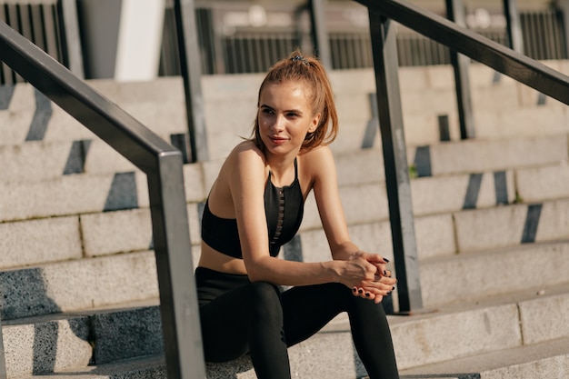 Европейская женщина в спортивной форме сидит на лестнице и готовится к тренировке на открытом воздухе