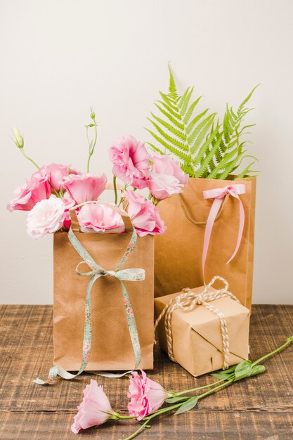 Eustoma flowers in brown paper bag with gift box on wooden surface against white wall