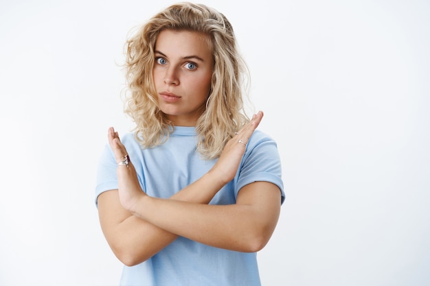 Not even think about it. Portrait of serious-looking displeased and intense bossy blond female with short curly haircut and blue eyes expressing disagreement showing cross gesture in prohibition