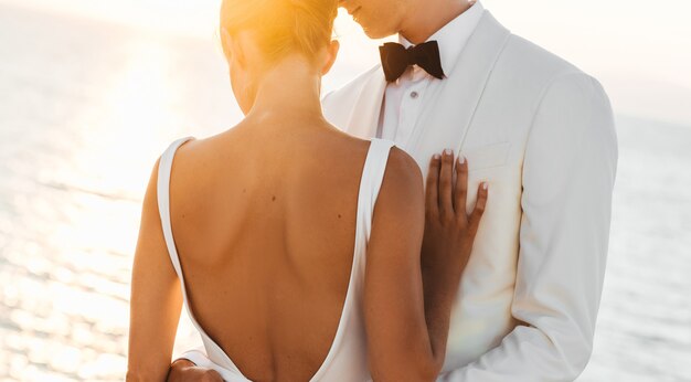 Evening sun shines over beautiful wedding couple hugging before the sea