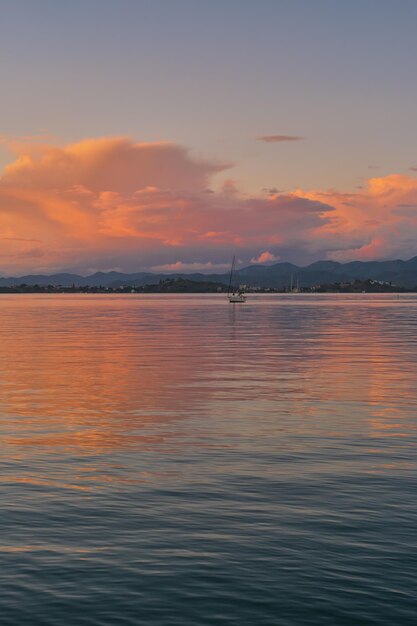 エーゲ海の垂直フレームの湾の夕方の暖かい風景には、山の範囲の背景がぼやけ、太陽の光の中で積雲の雲が背景のアイデアに