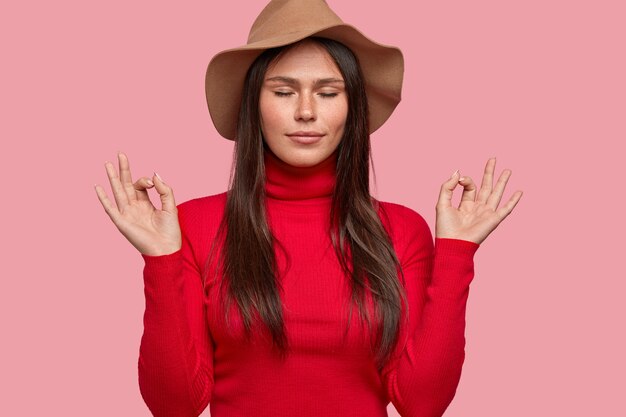 Everything is perfect. Relaxed freckled woman dressed in hat and red turtleneck sweater