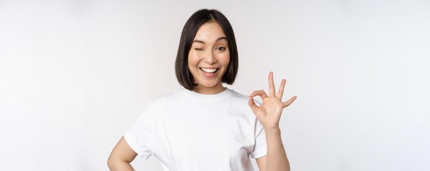 Everything okay Smiling young asian woman assuring showing ok sign with satisfied face standing over white background