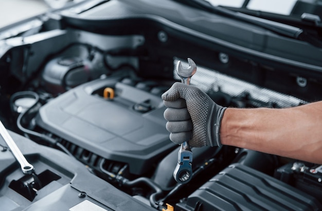 Everything will be fixed. Man's hand in glove holds wrench in front of broken automobile