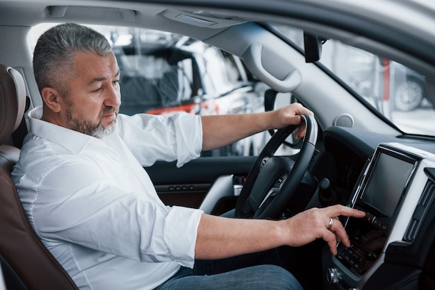 Everything working perfectly. Senior businessman in official clothes sits in a luxury car and pushing the buttons on the music player