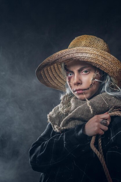 Evil creepy scarecrow concept - young woman in mist and smoke is posing for photographer.