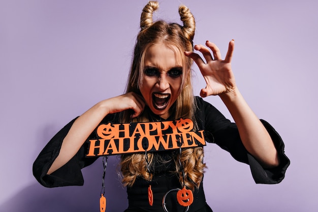 Злая ведьма смешно позирует в хэллоуин. Блондинка весело на карнавальной вечеринке.