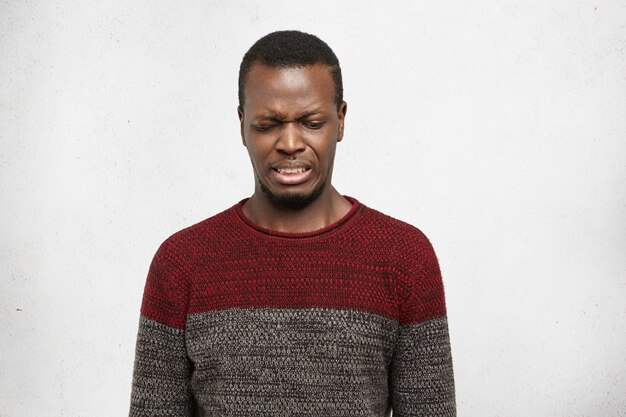 Eww. Headshot of disgusted or contempted young African American man looking down, feeling loathing and aversion towards something, making wry mouth, having fastidious and squeamish expression