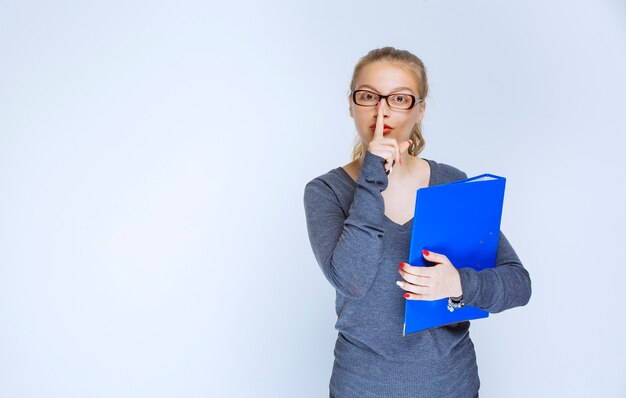 Exam assistant with a blue folder asking for silence.