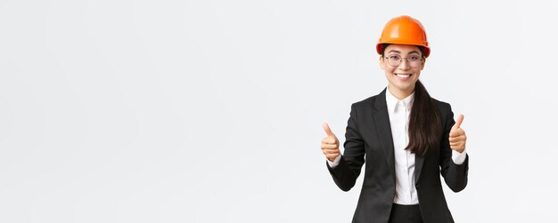 Отличная работа, хорошая работа Удовлетворенная профессиональная женщина-инженер, архитектор-строитель в защитном шлеме и костюме, показывающая большой палец в знак одобрения, рекламирует дом на продажу на белом фоне