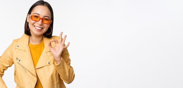 Excellent Smiling asian girl shows okay ok sign nod in approval recommending smth good standing over white background Copy space