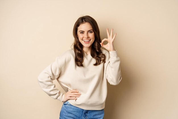 Excellent. Smiling beautiful woman showing okay, ok zero sign, approve smth good, praising and complimenting, beige background