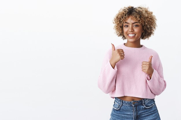 excellent, thumbs up to you. good-looking supportive and charismatic african american female friend with blond afro haircut showing like and great gesture as smiling, cheering over white wall