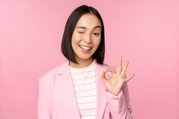 Excellent work well done gesture Smiling asian businesswoman showing okay ok sign praise good work recommending company looking as confident professional pink background