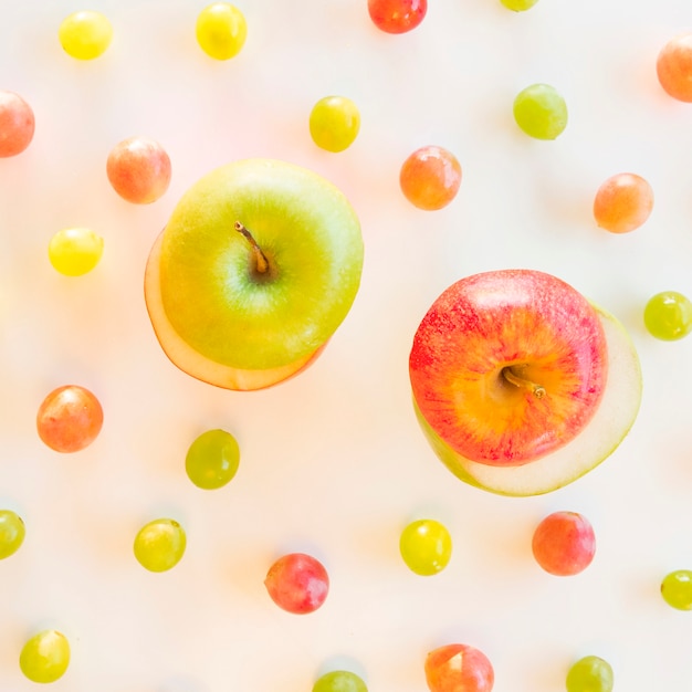 Обмен ломтиками зеленого и красного яблока в окружении винограда на белом фоне