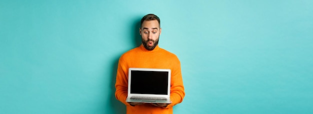 Free photo excited adult male model showing laptop screen demonstrating online promo standing happy against lig