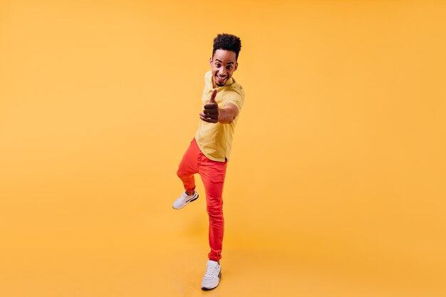 Excited african male model standing on one leg and laughing. Portrait of amazing smiling young man wears white sneakers.