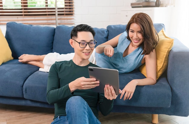 家の家族のライフスタイルの概念でソファで一緒にタブレットを使用して興奮しているアジアのカップルの男性と女性