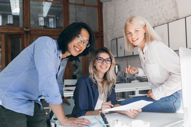 Excited asian student in blue shirt preparing for exams with caucasian female girl in glasses