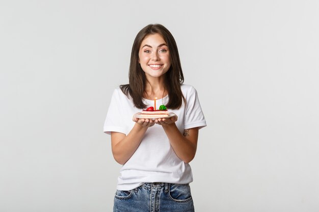 Excited attractive brunette b-day girl making wish on birthday cake, white.