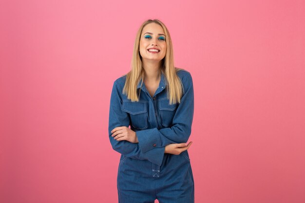 Excited attractive girl posing on pink background in denim overall fashion trend