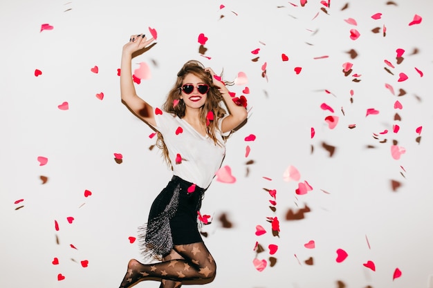 Excited barefooted woman jumping under heart confetti