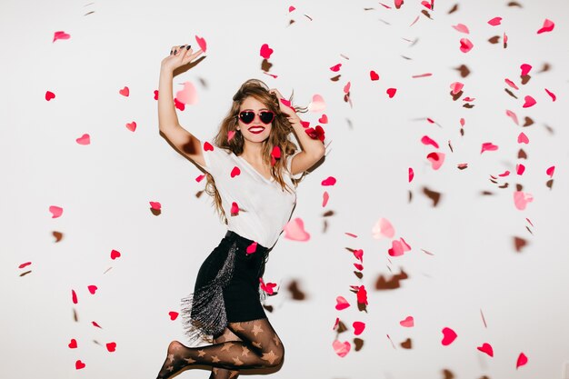 Excited barefooted woman jumping under heart confetti