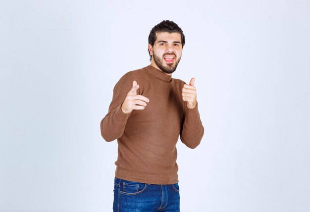 Excited bearded man in brown sweater pointing fingers at camera isolated on a white background. High quality photo