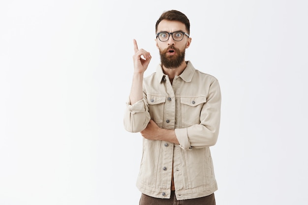 Excited bearded man in glasses posing against the white wall