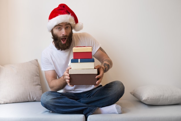 Excited bearded man wearing Santa hat and holding gift boxes