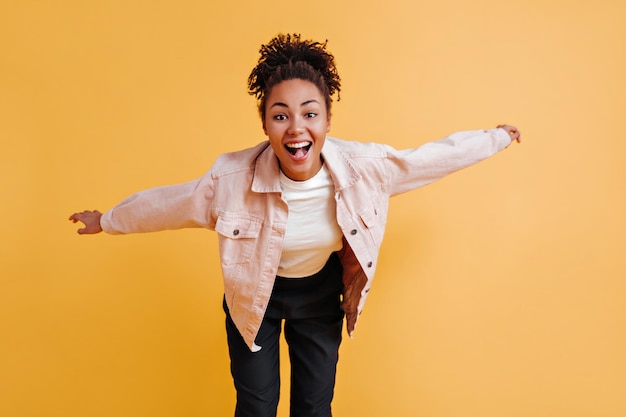 Excited beautiful black woman looking at camera African american girl in jacket laughing isolated on yellow background