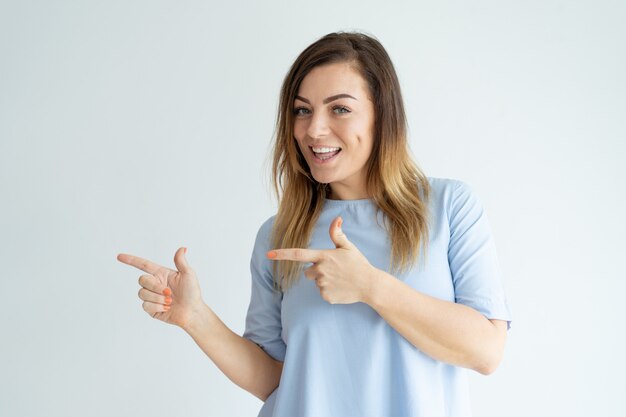 Excited beautiful woman pointing aside with both forefingers. 